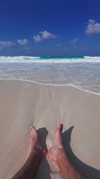Personal point of view of man sitting on sandy beach. Tide waves slightly splash to male feet. Man seats on the beach wide angle real time footage. North Coast of Egypt, Marsa Matrouh governorate