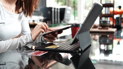 Close-up of hands holding a credit card and smartphone with a laptop and coffee cup in the background, symbolizing online payment.
