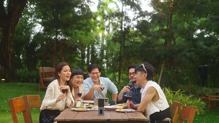Group of Happy Asian people diverse friends using mobile phone video recording together while celebration social gathering meeting dinner party eating food, drinking wine in the garden in evening. - Powered by Adobe