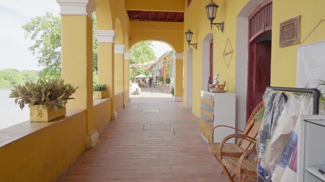 Point of view shot slowly moving through a yellow colonial arcade next to a river in mompox