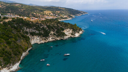 Fototapeta premium Zakynthos Greece aerial view of sandy beach with umbrellas rocky coastline and crystal clear Ionian Sea with yachts sailing in blue water