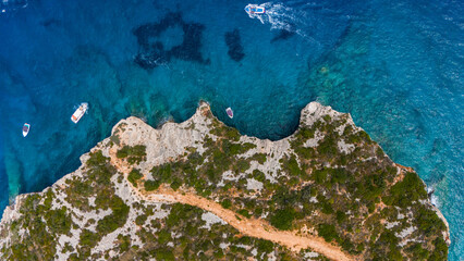 Blue Caves entrance Zakynthos Greece aerial top view of rocky peninsula with path green vegetation turquoise Ionian Sea and boats near coastline