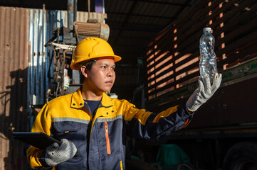 Plastic bottle and worker: A worker in a yellow helmet and blue-yellow jacket examines a plastic bottle, with a thoughtful expression, and an industrial backdrop.