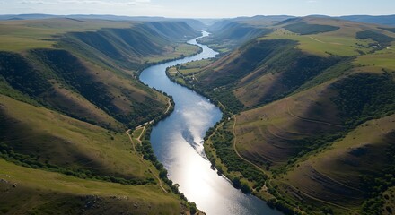Aerial view of a winding river cutting through rolling green hills and valleys