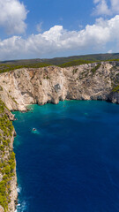 Turquoise bay surrounded by high limestone cliffs and forested hills with deep blue Ionian Sea stretching to the horizon under cloudy summer sky