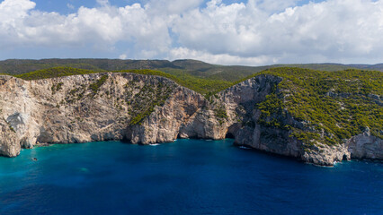 Aerial coastline view with dramatic cliffs forested slopes turquoise coves and deep blue Ionian Sea reflecting clouds across the summer horizon