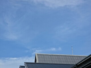 Fototapeta premium a bright blue sky with thin, wispy cirrus clouds above the sloped, corrugated metal roofs of several buildings.