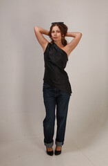 Full length studio portrait of beautiful young brunette woman in black trousers and shirt on gray background