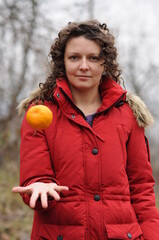Curly girl in a red jacket tosses an orange