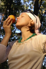 A girl is holding and smelling a peach.