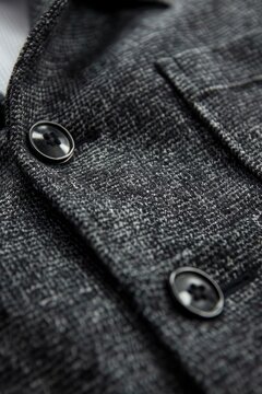 Close-up of a dark gray textured knit fabric garment, showcasing a buttoned placket and a small pocket.  The material has a subtle heathered pattern