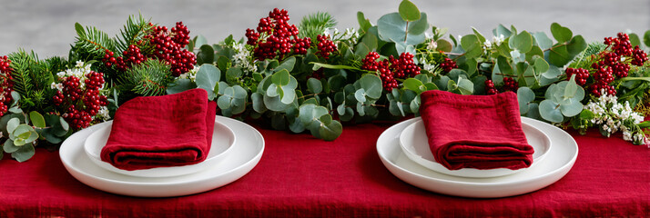 Elegant holiday table setting with eucalyptus runner and red napkins, wide bottom copy space for menu