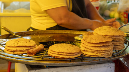 A woman is cooking food on a grill. There are several tortillas on the grill. Historic center of...