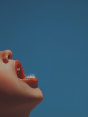 Artistic close-up of a person?s mouth open against a clear blue sky, showcasing red lips and a playful expression.
