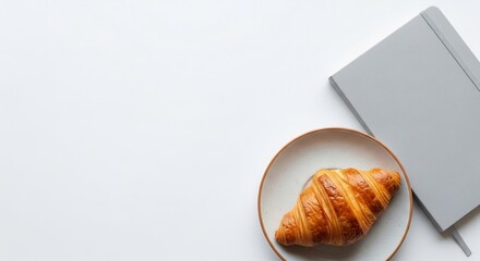 Golden Croissant on Speckled Plate Beside Gray Notebook with Elastic Band