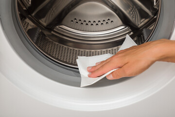 Young adult woman hand holding dry paper napkin and wiping door sealing rubber inside white washing...
