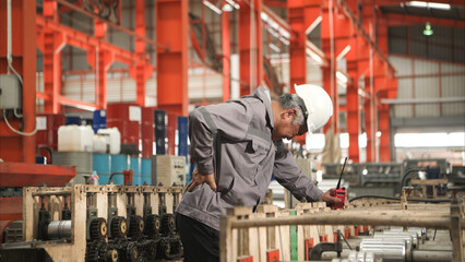 Industrial worker in protective gear experiencing back pain while working on factory machinery