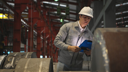 Industrial worker inspecting inside a large metal tube in a factory wearing safety helmet