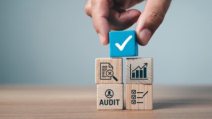 Hand places a blue block with a white checkmark on top of wooden blocks representing business concepts like audit and growth