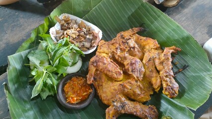 Traditional Indonesian grilled chicken served on banana leaf with sambal, vegetables, and sides. Perfect for culinary, cultural, heritage, or rustic-themed visual content