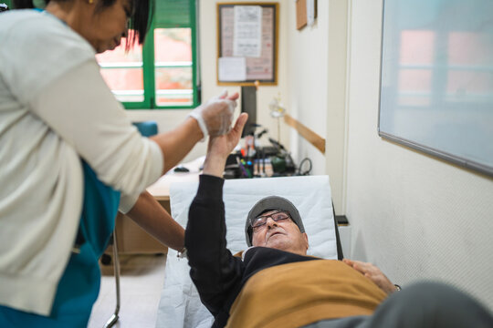 Healthcare professional assisting an elderly man performing physical therapy exercises while lying on a gurney in a care facility - Powered by Adobe
