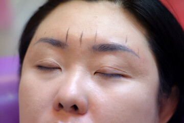 The tattoo artist is drawing the eyebrows of a customer.