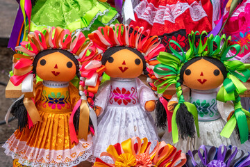 Three dolls with colorful hair and dresses are displayed on a table. The dolls are arranged in a...