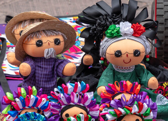 A group of dolls with colorful ribbons around their heads. The dolls are of a man and a woman. Historic center of Queretaro City, decorations and traditions to celebrate Mexico's Independence Day, col