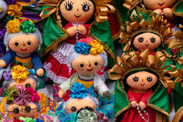 A collection of dolls with colorful clothing and flower decorations. The dolls are arranged in a row. Historic center of Queretaro City, decorations and traditions to celebrate Mexico's Independence D