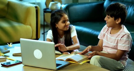 Indian small brother sister studying at home with laptop textbook, notepad indoors, Asian young kids siblings learning together using computer technology in modern living room, education and homework - Powered by Adobe