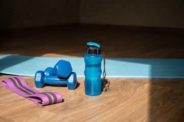 Dumbbells resistance band and water bottle on yoga mat at home
