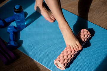 Female legs on foam roller doing myofascial massage with dumbbells and water bottle nearby
