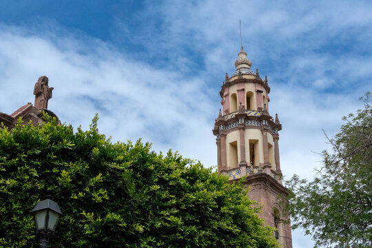 A tall building with a clock tower and a cross on top. The sky is blue and the sun is shining. Historic center of Queretaro City, decorations and traditions to celebrate Mexico's Independence Day, col
