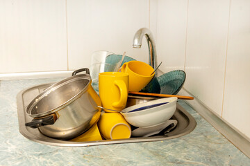 Dirty and unwashed dishes are stacked in the kitchen sink. Unwashed cups, plates, pots, forks and...