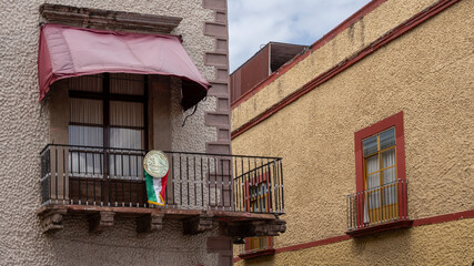A balcony with a red awning and a clock on it. The balcony is on the side of a building. Historic center of Queretaro City, decorations and traditions to celebrate Mexico's Independence Day, colonial 