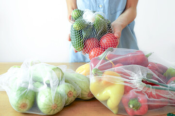 Autumn harvest in eco-friendly packaging: seasonal vegetables and a woman holding cucumbers and tomatoes in a mesh bag. Farm-to-table lifestyle. Seasonal eating and local food movement concept.