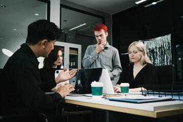 Four colleagues engage in a collaborative office meeting, using laptops, tablets, and documents to brainstorm ideas, discuss strategies,share insights, fostering teamwork, productivity, professional