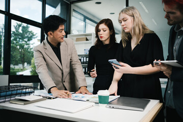Four colleagues engage in a collaborative office meeting, using laptops, tablets, and documents to brainstorm ideas, discuss strategies,share insights, fostering teamwork, productivity, professional