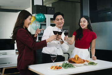 Four cheerful friends celebrate together in an office party, enjoying delicious food, fried chicken, pizza, salad, wine. Surrounded by balloons and laughter, they share happiness, marking   year-end