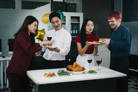 Four cheerful friends celebrate together in an office party, enjoying delicious food, fried chicken, pizza, salad, wine. Surrounded by balloons and laughter, they share happiness, marking   year-end