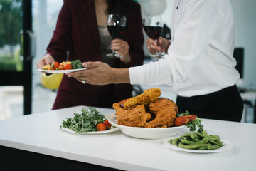 Four cheerful friends celebrate together in an office party, enjoying delicious food, fried chicken, pizza, salad, wine. Surrounded by balloons and laughter, they share happiness, marking   year-end