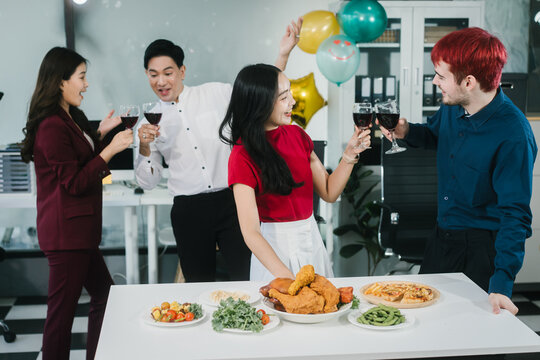 Four cheerful friends celebrate together in an office party, enjoying delicious food, fried chicken, pizza, salad, wine. Surrounded by balloons and laughter, they share happiness, marking   year-end - Powered by Adobe