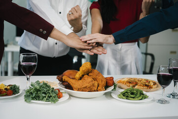 Four cheerful friends celebrate together in an office party, enjoying delicious food, fried chicken, pizza, salad, wine. Surrounded by balloons and laughter, they share happiness, marking   year-end