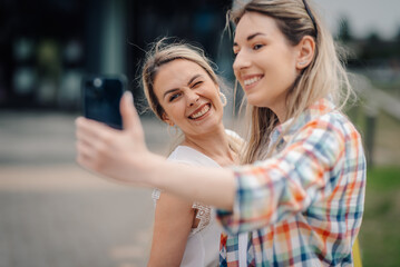 Obraz premium Two smiling women taking a selfie with smartphone outdoors