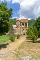 A grassy road with faded grass leads to a passage into the monastery courtyard through a high bell tower. The dome of the church is visible. Pitareti monastery. Georgia