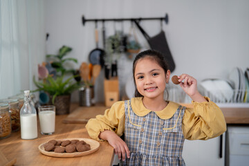 Portrait of Asian young girl eating delicious cookies in kitchen at home. 