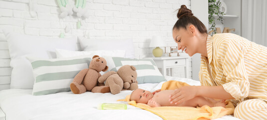 Beautiful young happy mother with cute little baby and bottle of shampoo after bathing in bedroom at home