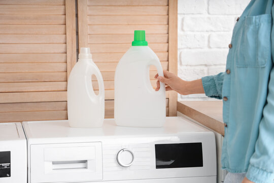 Young woman with bottle of detergent on washing machine in laundry room, closeup