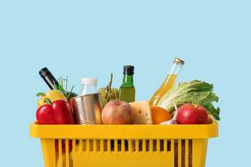 Yellow shopping basket full of different fresh products and apples on blue background