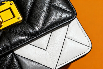 Close-up of a black and white quilted leather handbag with a gold-tone clasp against an orange background